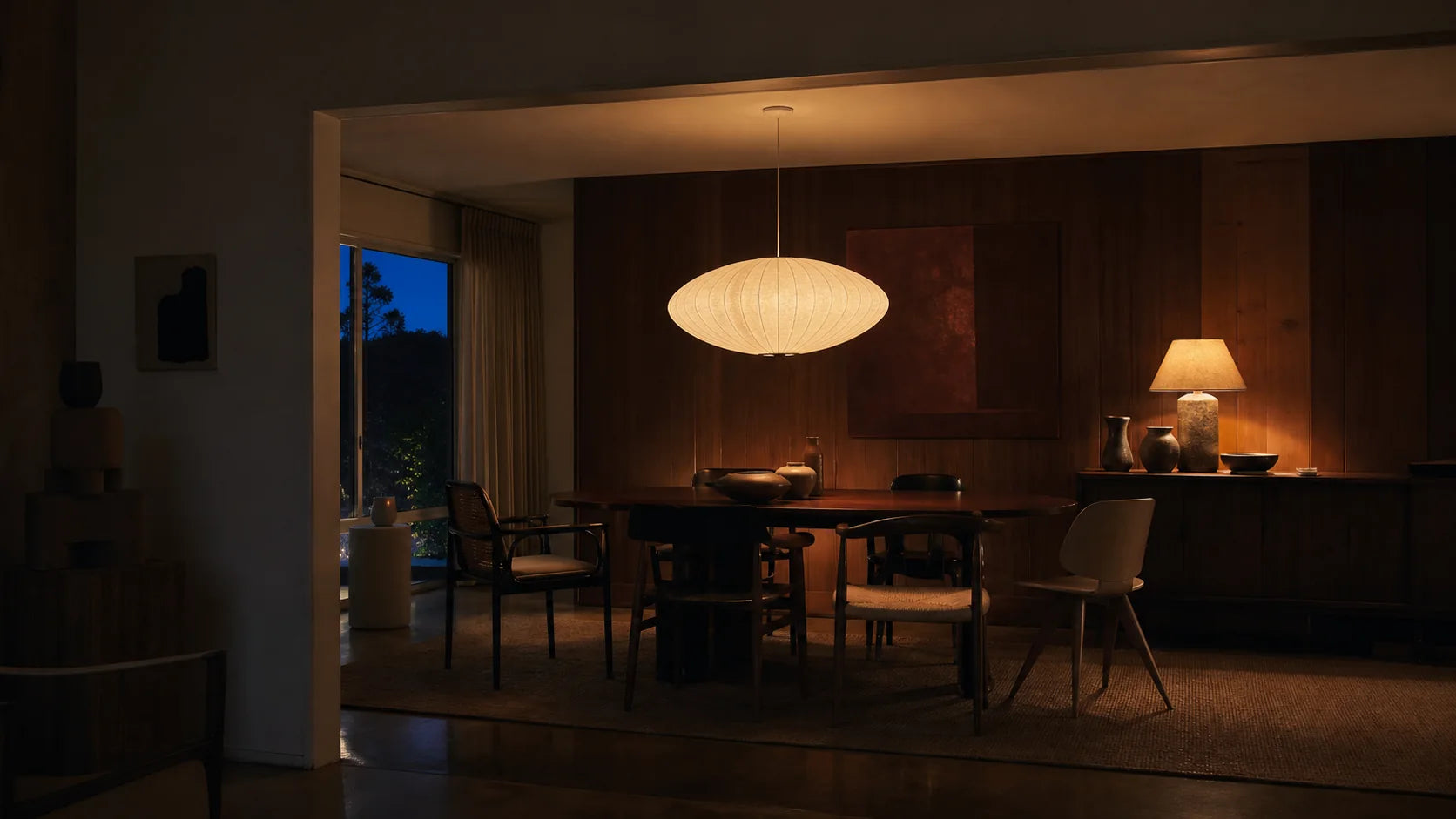 Warmly lit dining room with vintage chairs and sculptural lighting at blue hour