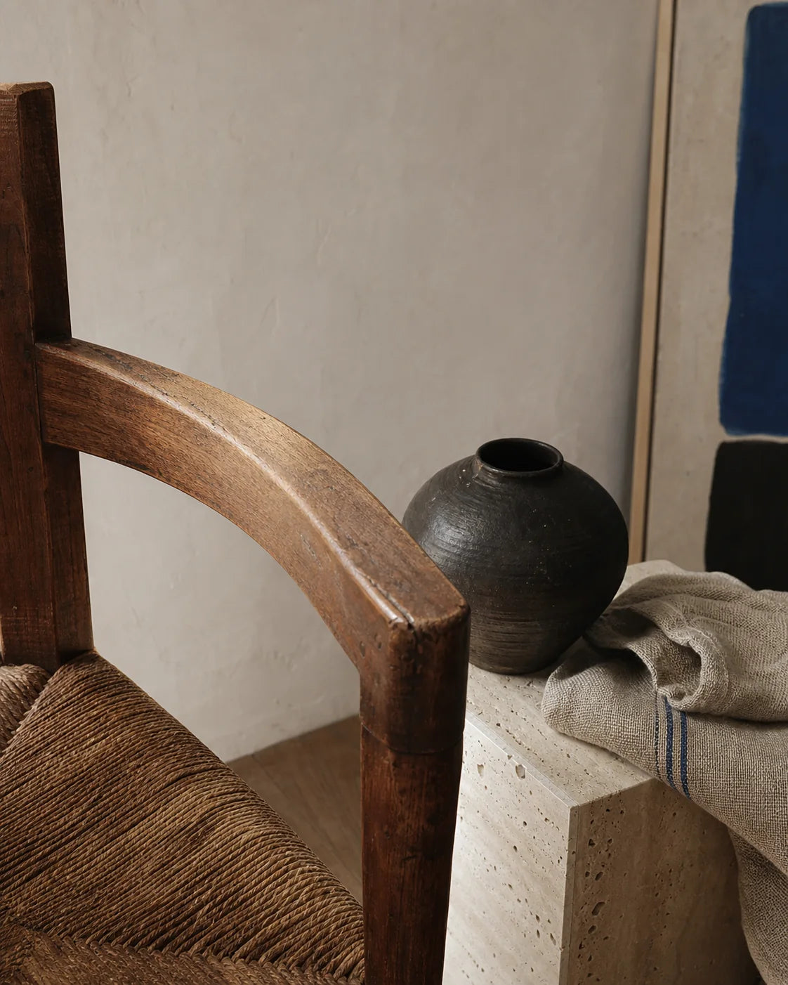 Close study of aged walnut, woven rush, travertine, linen, and ceramic